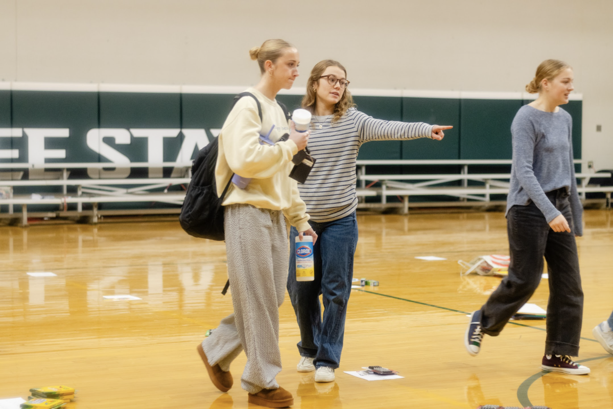 Pointing, NHS Director of Communications senior Greta Barnett shows senior Amelia Wiles where to place her items for donation.